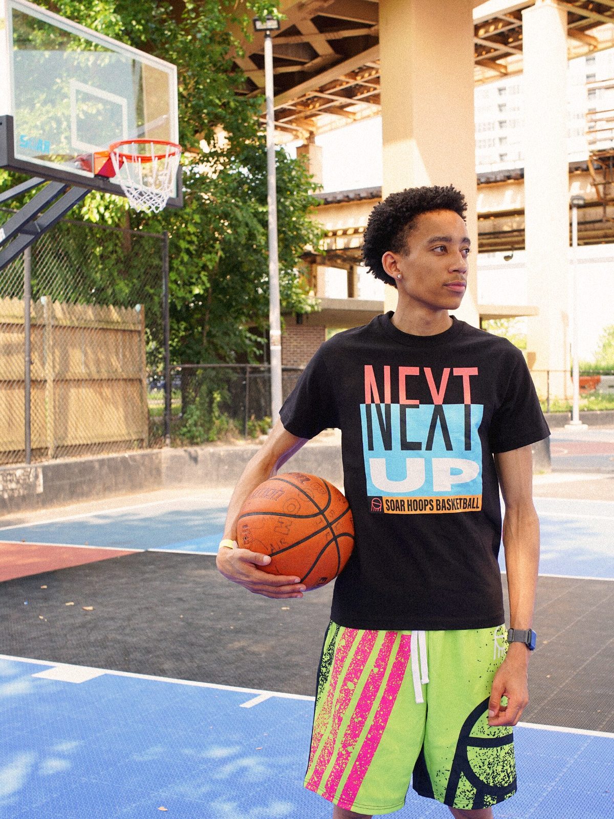 Player in SOAR Next Up tee and Fresh Paint neon shorts holding a basketball under the overpass court