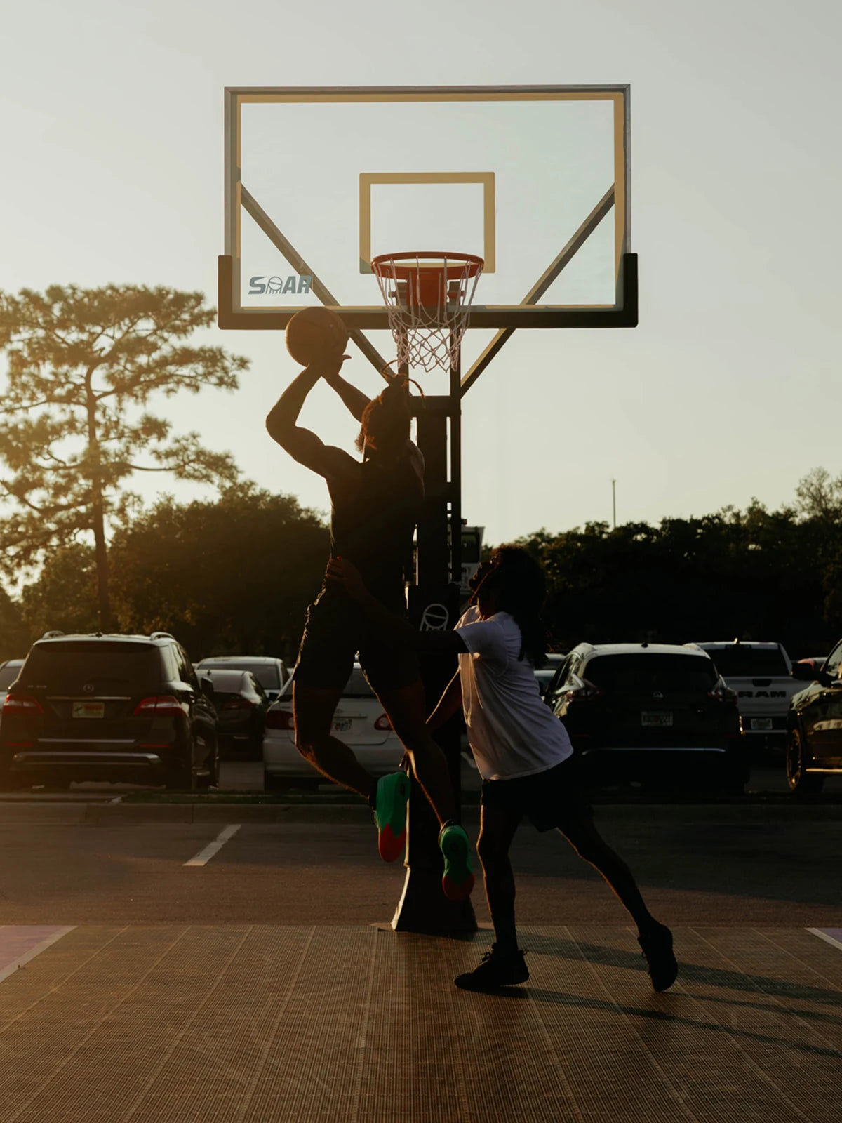 Two players playing basketball at a SOAR hoop in the evening